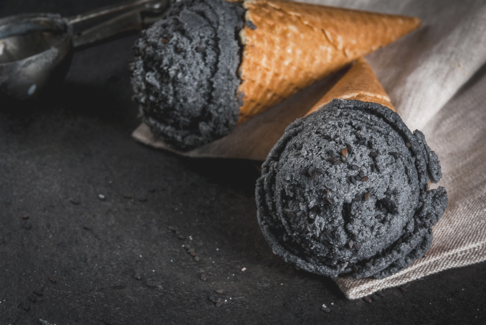 Trendy food. Black ice cream with black sesame, in traditional portioned ice cream cones. On a black stone table, in a wooden tray. Copy space