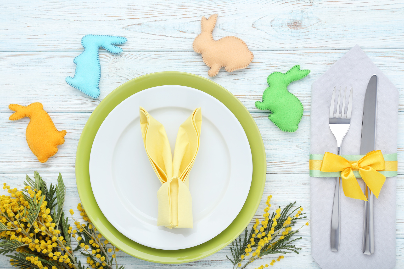 Kitchen cutlery with easter fabric rabbits and mimosa flowers on wooden table
