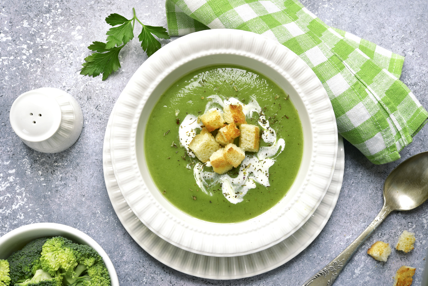 Broccoli pureed soup with croutons in a white plate on a light slate, stone or concrete background.Top view.